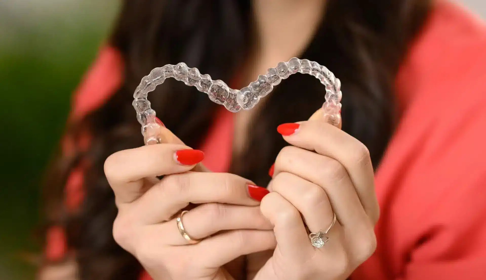 A Foxxi szakorvosa két kezében tartva szívet formál két kivehető sínes, láthatatlan Invisalign fogszabályozóból.